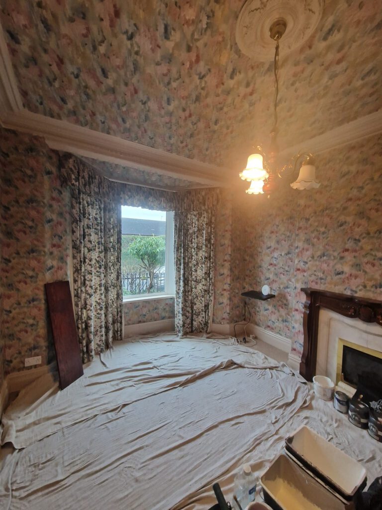 Before: front room with dated floral wallpaper, floor protected with dust sheets