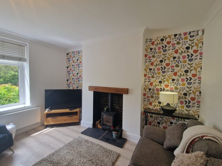 Living room with floral wallpaper in the chimney alcoves and a wood burner