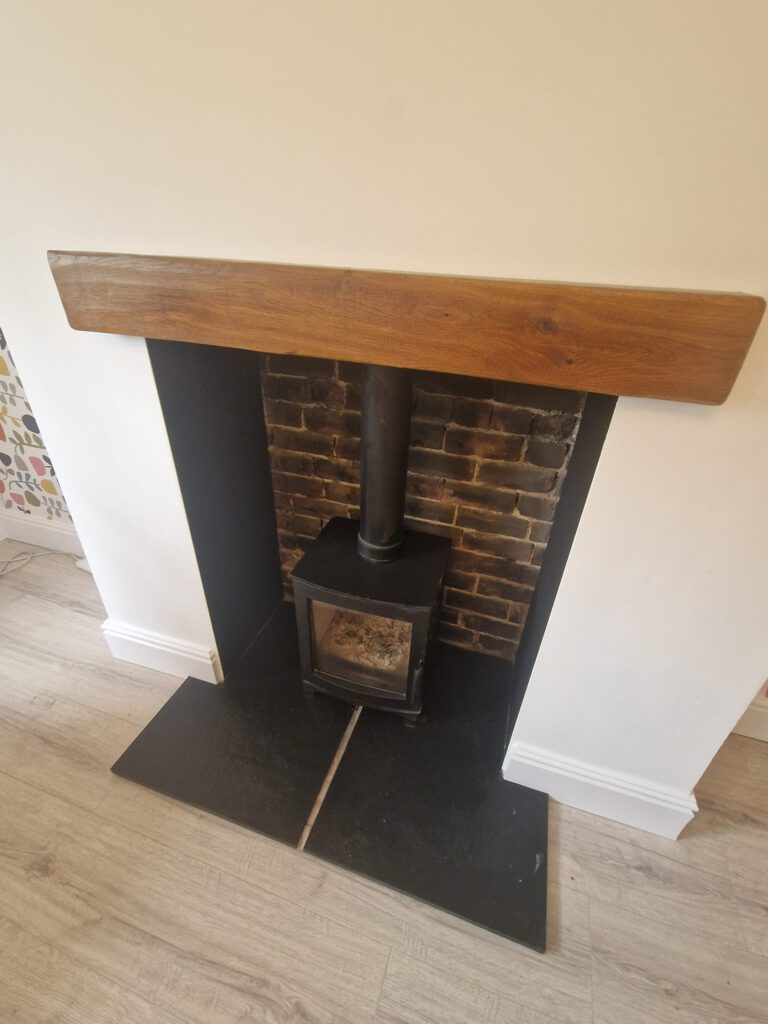 Chimney breast painted white around a wood burner with an oak beam mantel